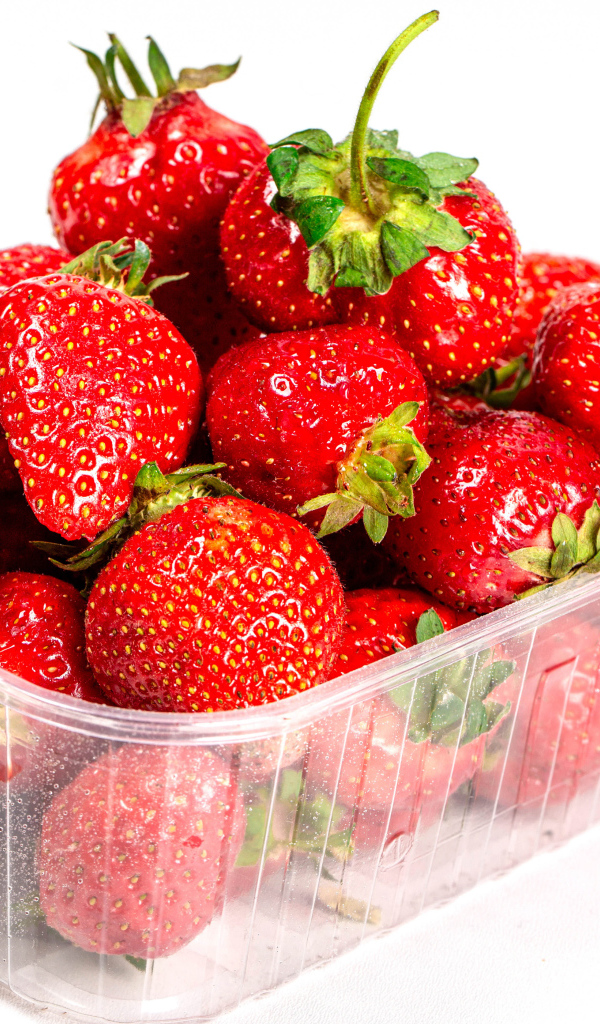 Спелая вкусная клубника в пластиковом контейнере на белом фоне