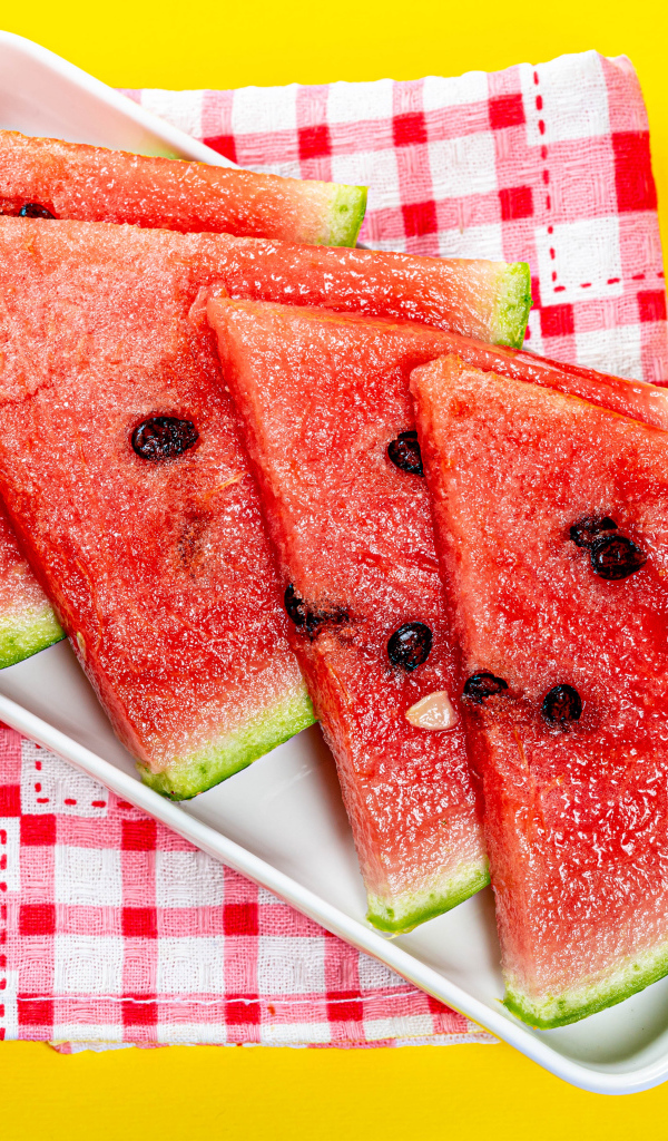 Кусочки сочного арбуза в тарелке на желтом столе