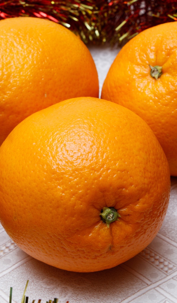 Три больших апельсина на столе с мишурой 