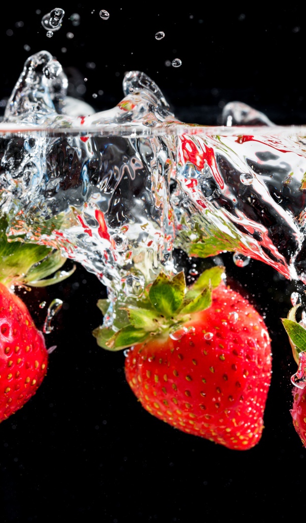Три ягоды клубники в воде на черном фоне