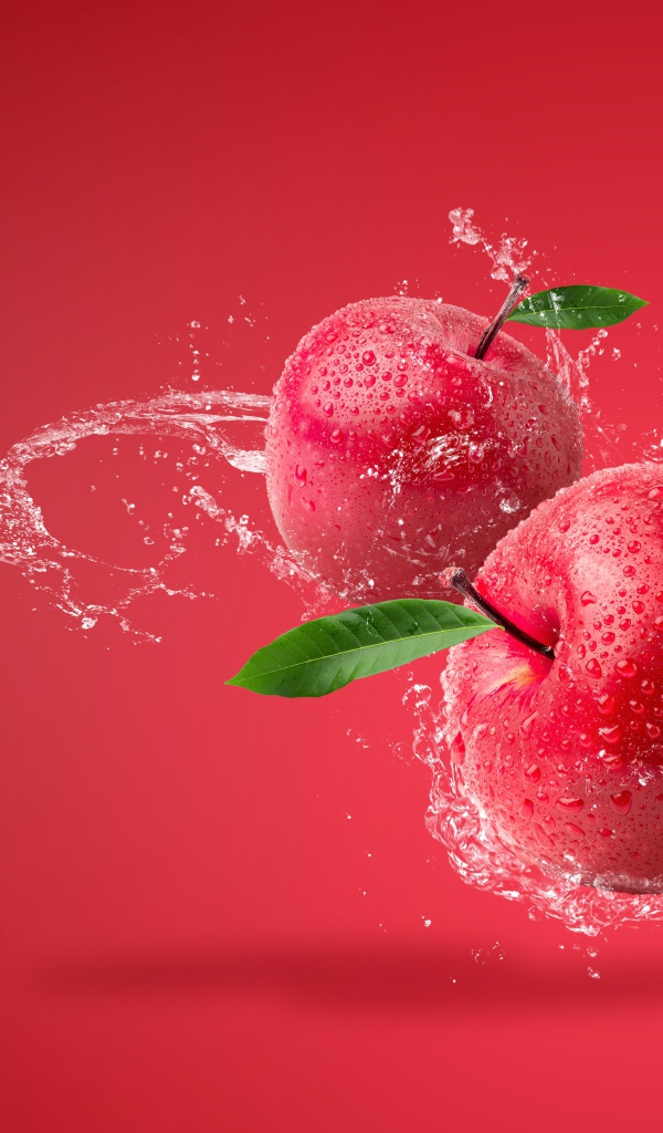 Два яблока в брызгах воды на красном фоне