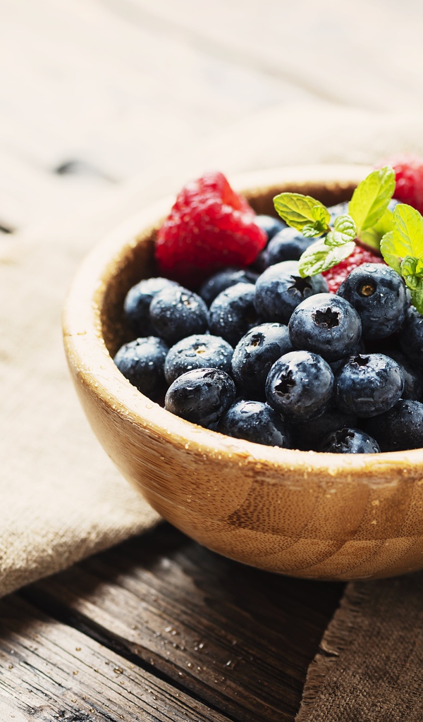 Мокрые ягоды черники в деревянной миске с малиной 