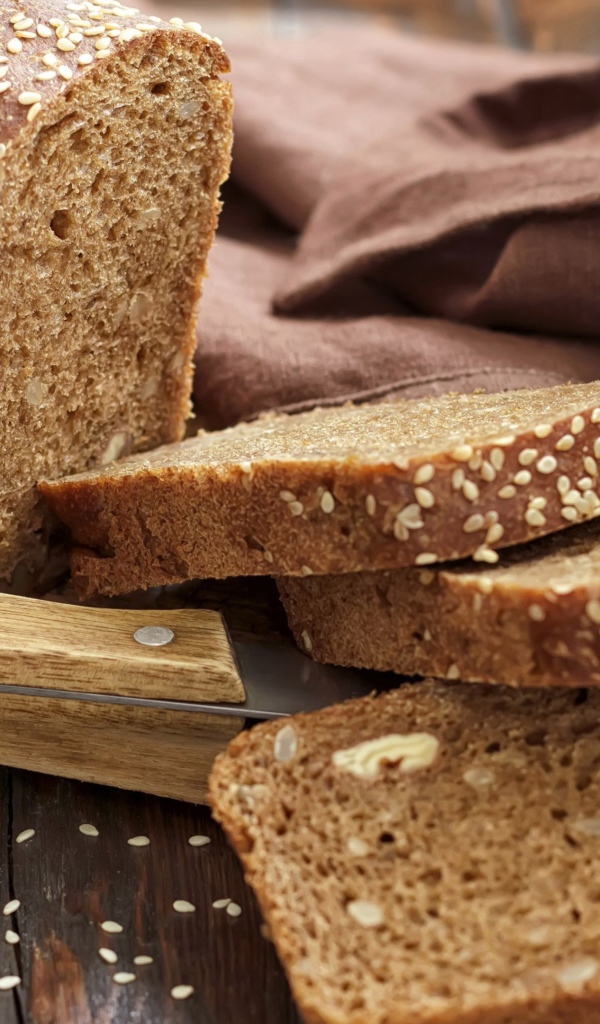 Буханка хлеба нарезанная кусочками на столе с ножом