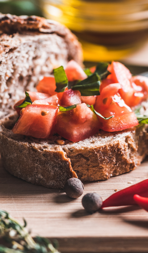 Черный хлеб с кусочками помидора на столе с острым красным перцем