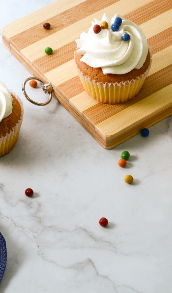 Кексы с кремом и разноцветными шариками на столе с доской