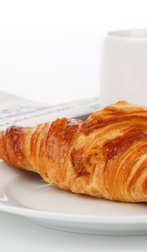 Свежий круассан лежит на белой тарелке с кофе 