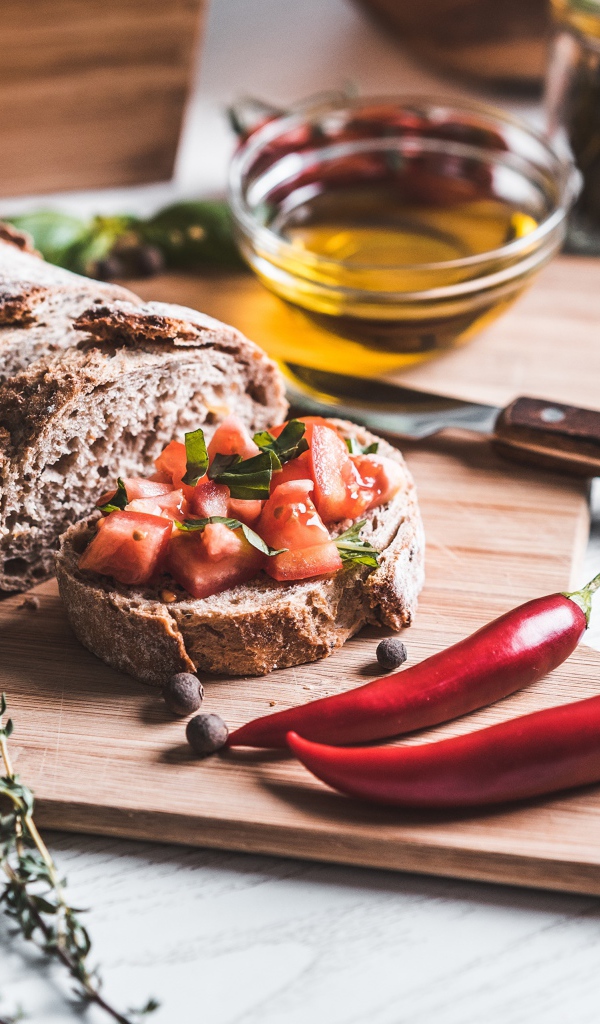 Батон с помидорами и красным перцем на столе с маслом