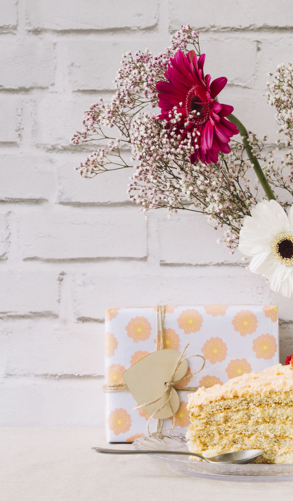 Кусок торта, подарок и букет на столе на фоне стены 