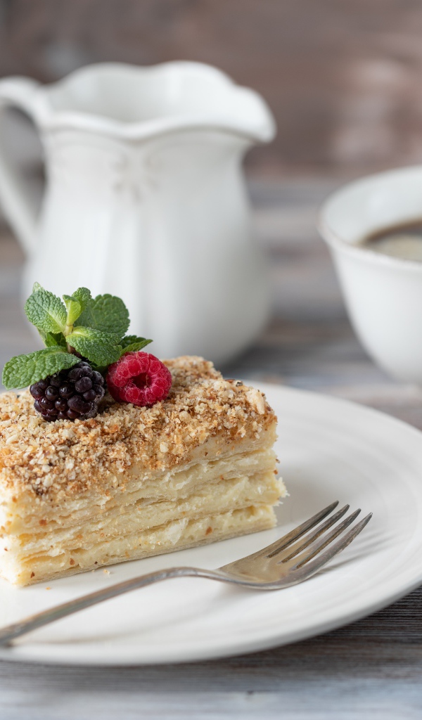 Кусок торта лежит на белой тарелке на столе с кофе