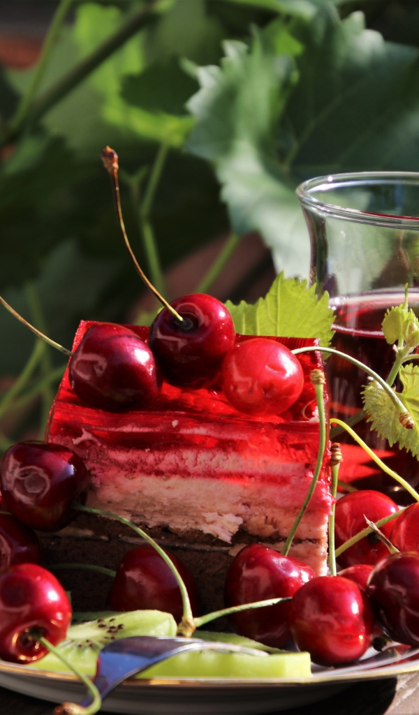 Кусок торта с черешней на столе с чашкой чая 