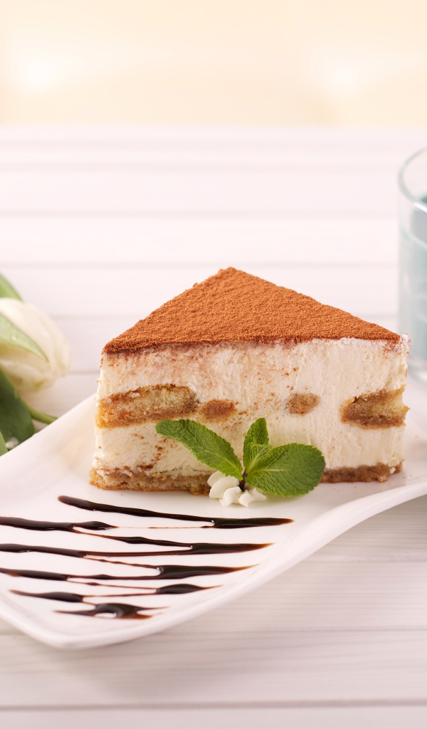 Кусок тирамису на столе с зажженными свечами и букетом тюльпанов