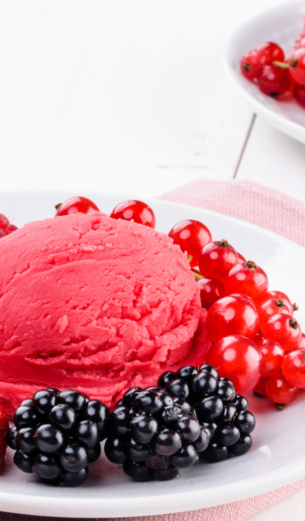 Шарик фруктового мороженого с ягодами на белой тарелке