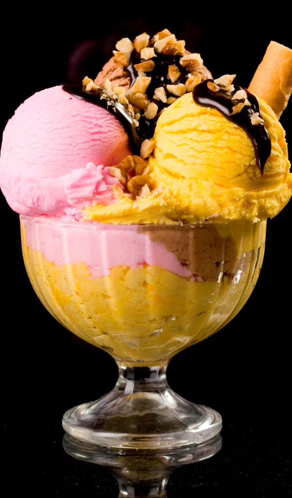 Шарики фруктового мороженого в креманке с орехами и шоколадом на черном фоне