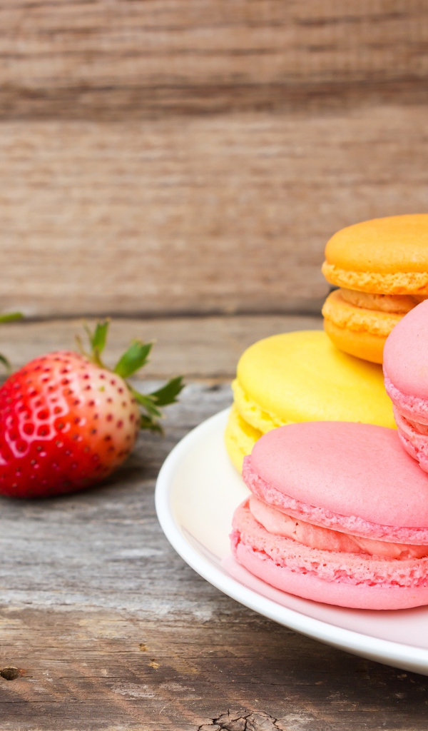 Разноцветный десерт макарун на белой тарелке на столе с клубникой