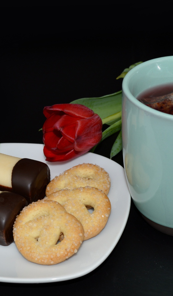 Печенье с конфетами на столе с чашкой чая и тюльпаном