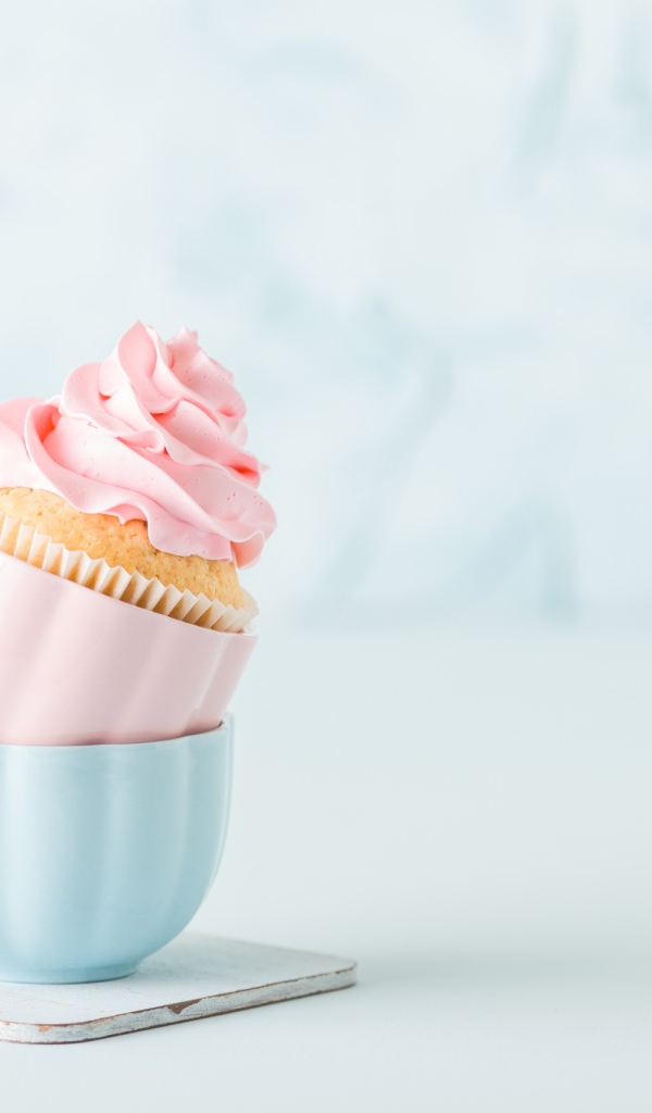 Кекс с розовым кремом с чашками на столе 