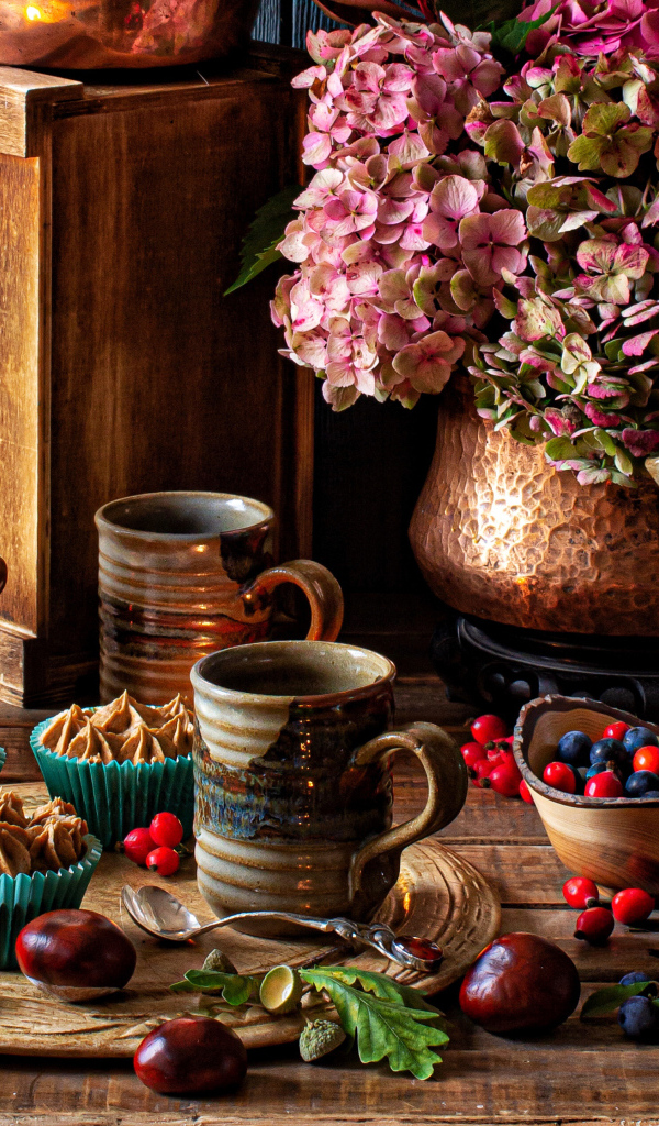 Кексы с кремом на столе с ягодами, цветами и лампой 