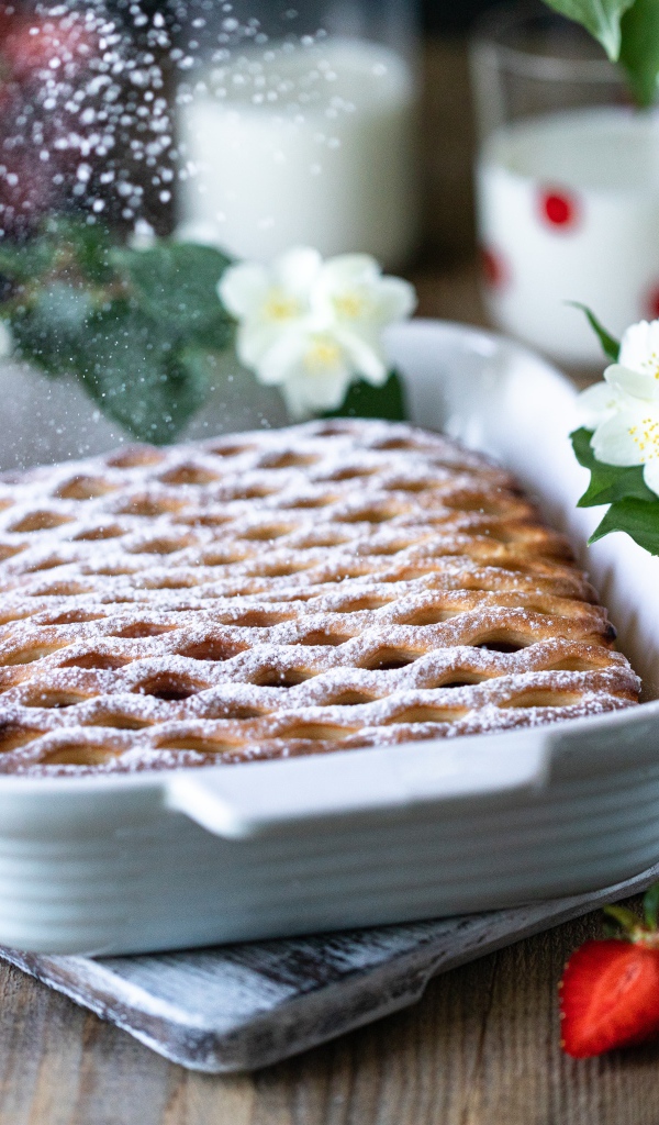 Вкусный клубничный пирог с сахарной пудрой на столе с цветами жасмина