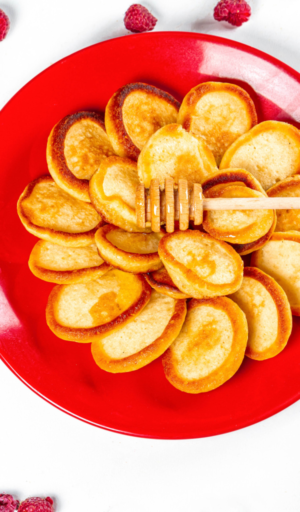 Оладьи на красной с медом на красной тарелке на столе с ягодами малины