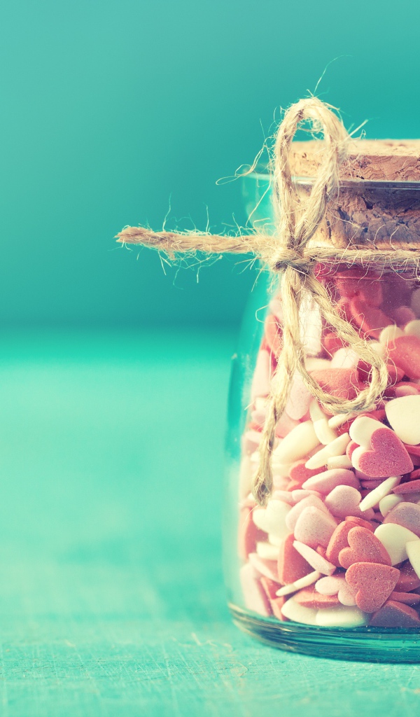 Стеклянная банка с маленькими конфетами в форме сердца на голубом фоне