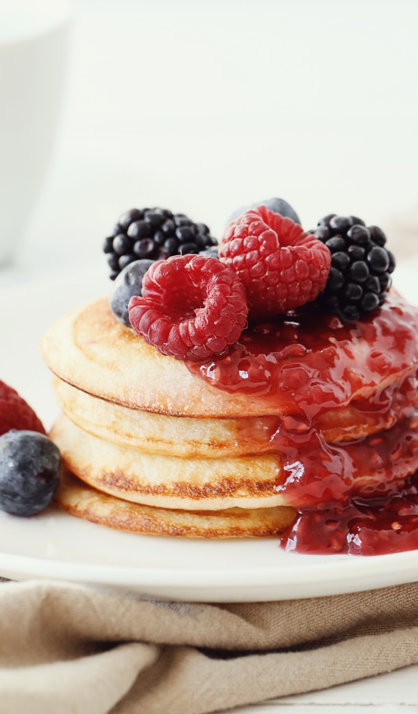 Оладьи на большой белой тарелке с джемом и ягодами 