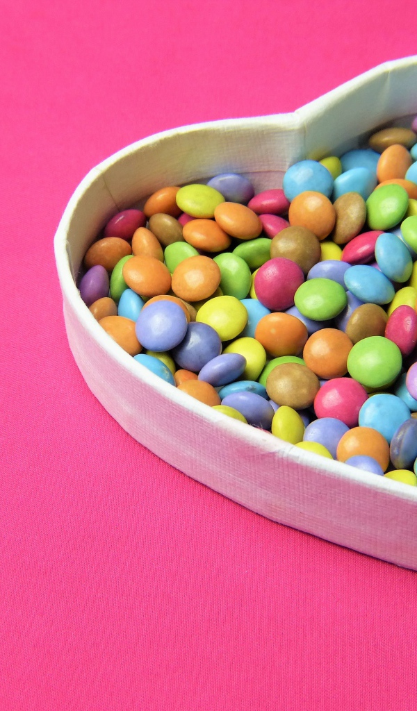 Коробка в форме сердца с разноцветными конфетами на розовом фоне