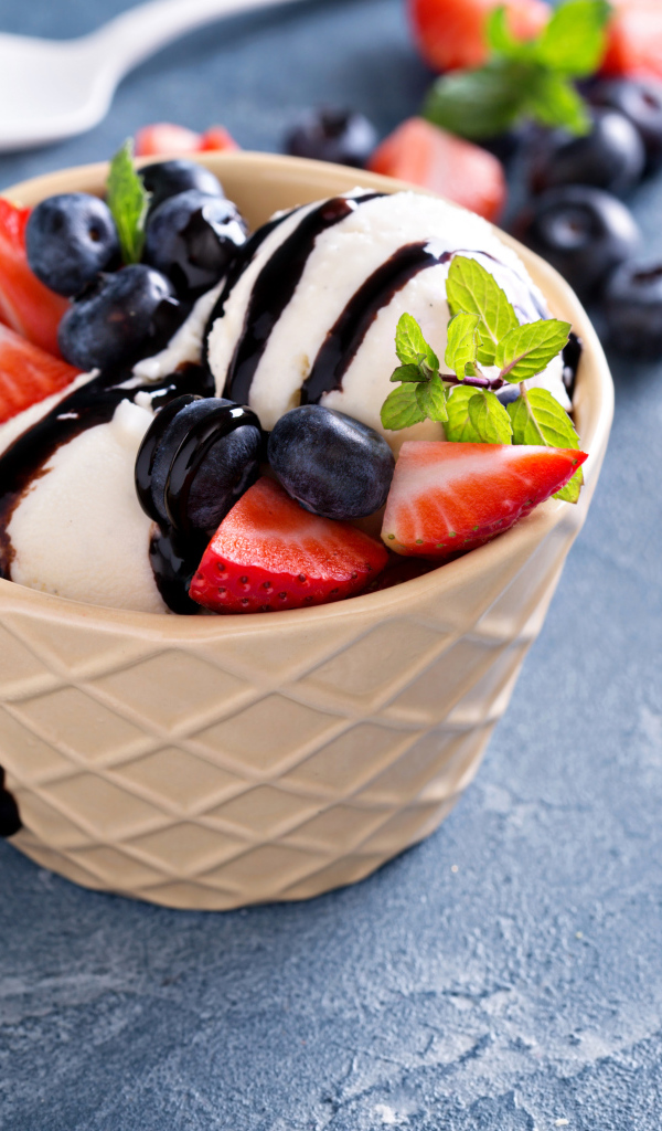 Шарики мороженого в стакане на столе с клубникой и ягодами черники