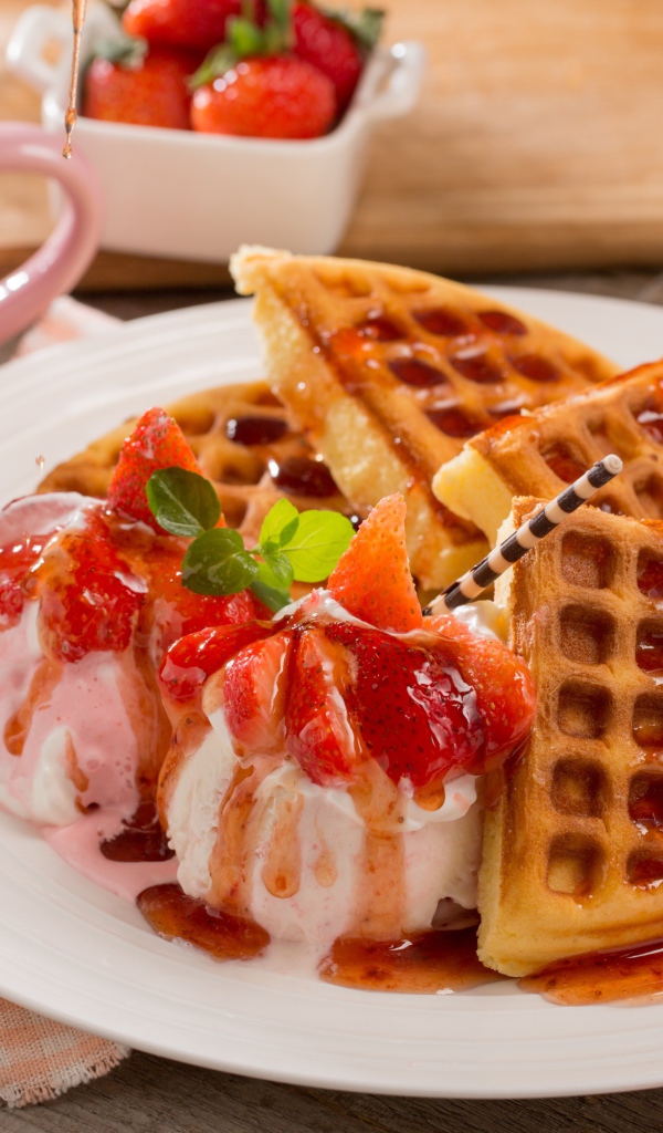 Шарики мороженого с клубникой на тарелке с вафлями и сиропом 