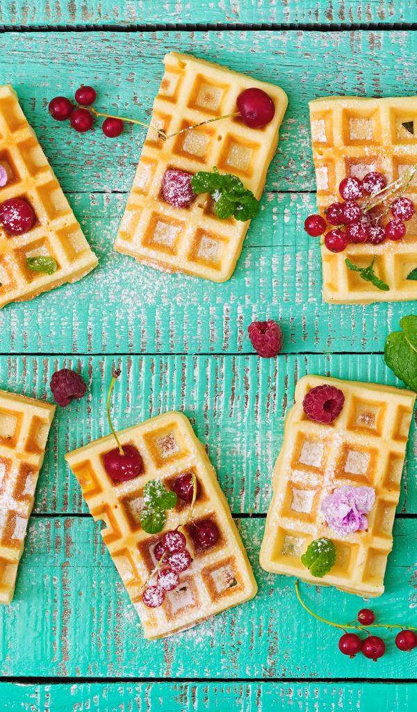 Большие сладкие вафли с ягодами и сахарной пудрой на столе 