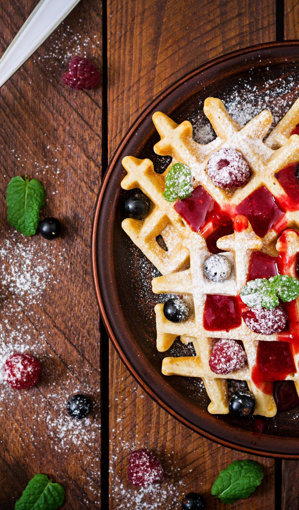 Сладкие медовые вафли на тарелке с ягодами и джемом и сахарной пудрой 