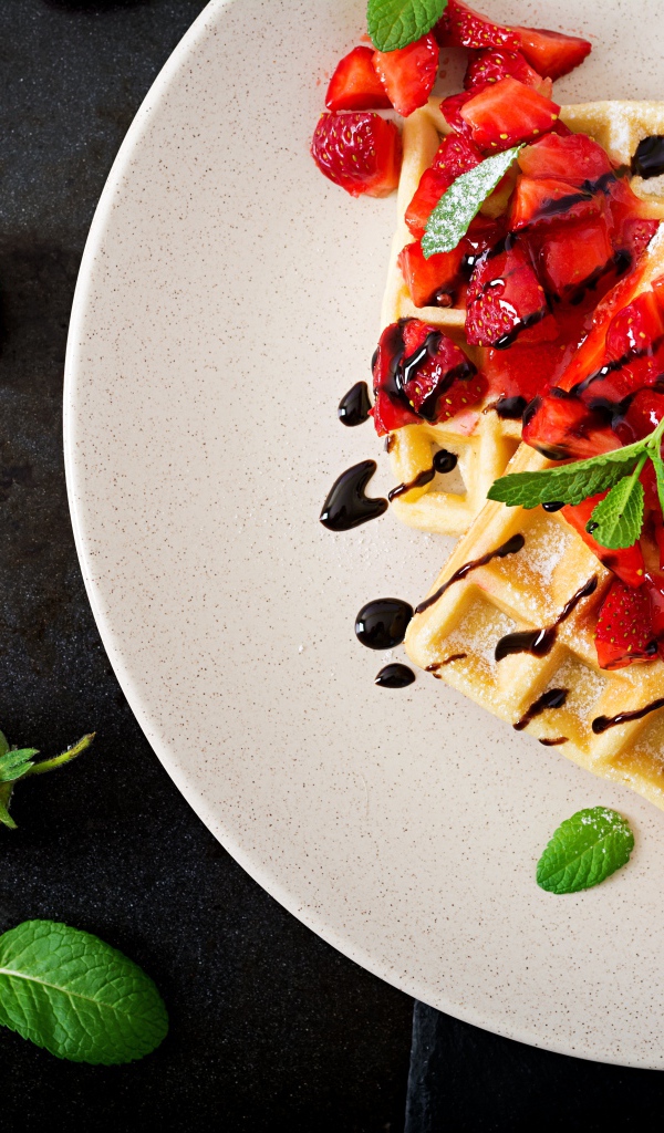 Сладкие вафли на тарелке с кусочками клубники