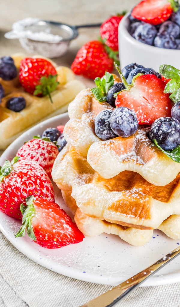 Вкусные сладкие вафли с ягодами клубники, черники и сахарной пудрой