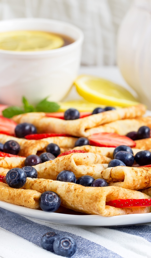 Тонкие блинчики с ягодами черники и клубники на столе с чаем