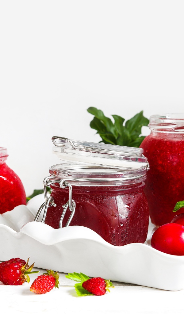 Три банки джема с ягодами на белом фоне