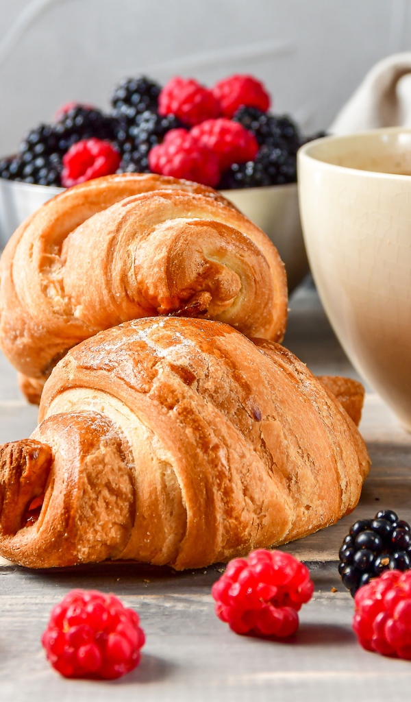 Два круассана на столе с чашкой кофе и ягодами