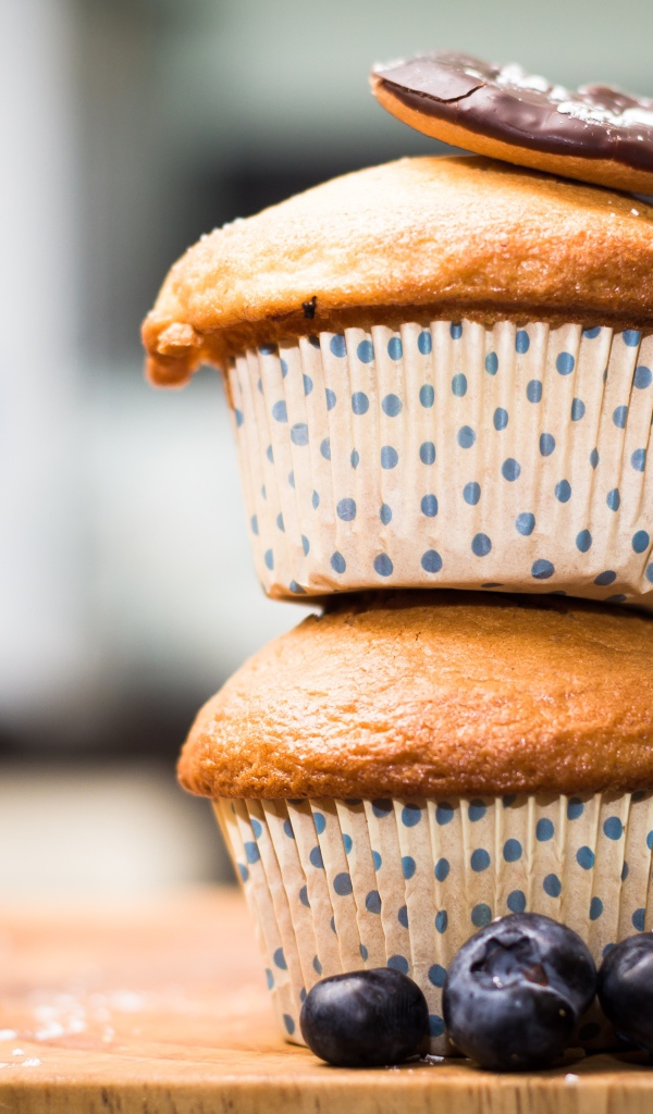 Два кекса стоят на столе с ягодами черники 