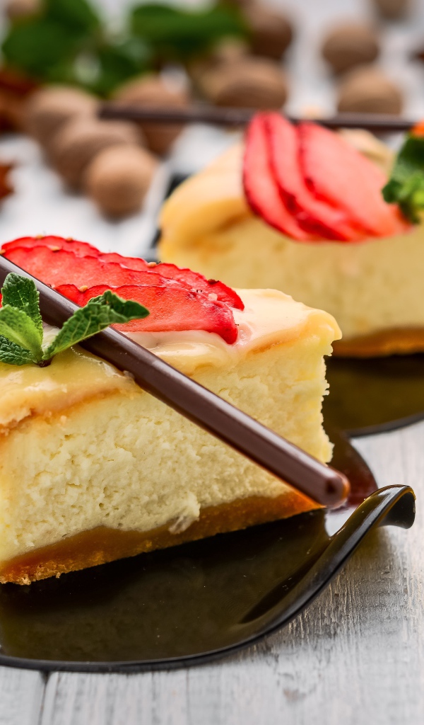 Два куска чизкейка с клубникой на столе с палочками