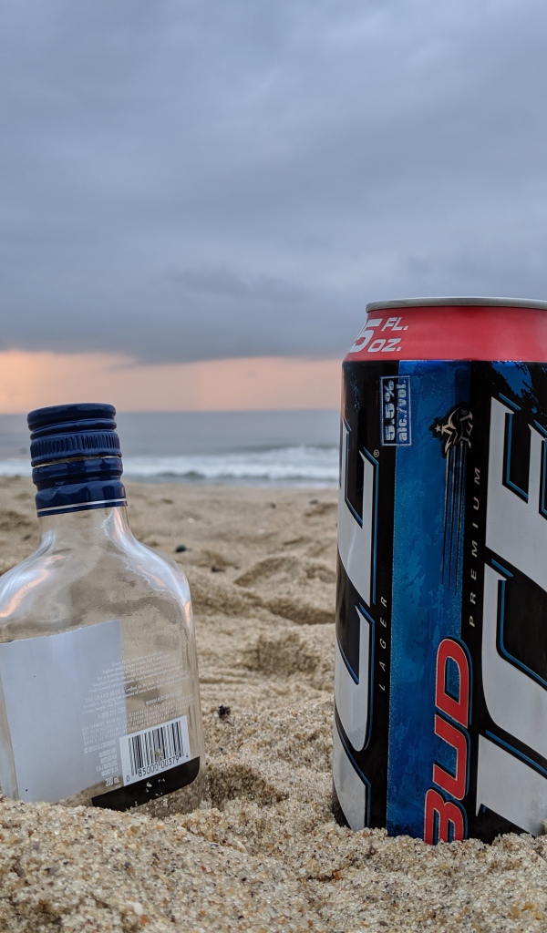 Бутылка пива и бутылка водки на песке у моря
