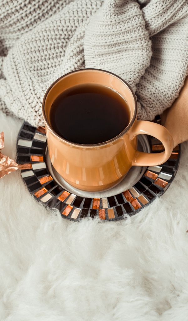 Чашка кофе стоит на покрывале с теплым свитером 