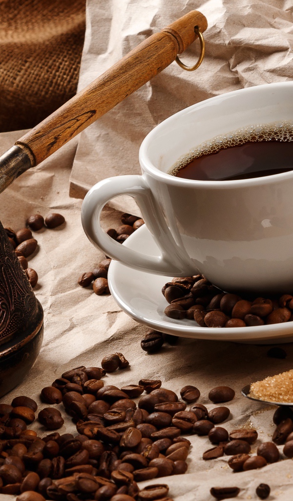 Чашка горячего кофе на столе с туркой, зернами и коричневым сахаром