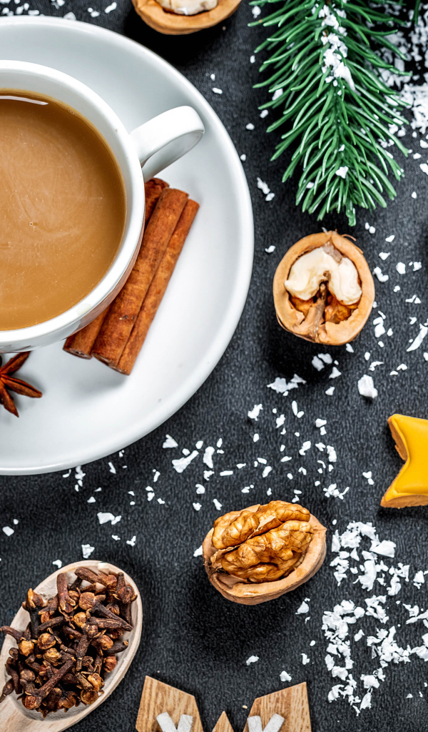 Чашка горячего кофе на столе с орехами и еловыми ветками 