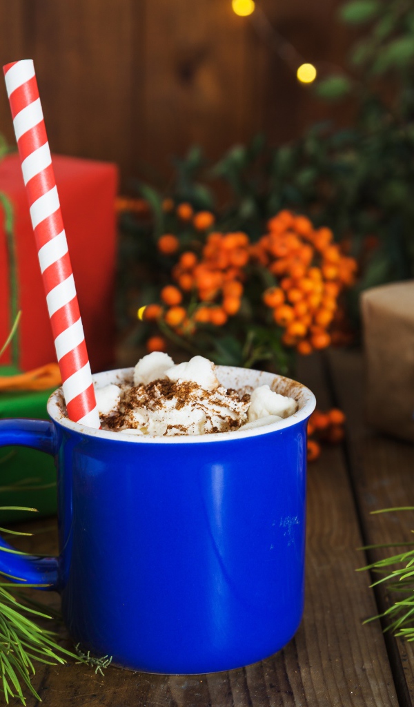 Синяя чашка горячего шоколада с маршмеллоу на столе с еловыми ветками и подарками