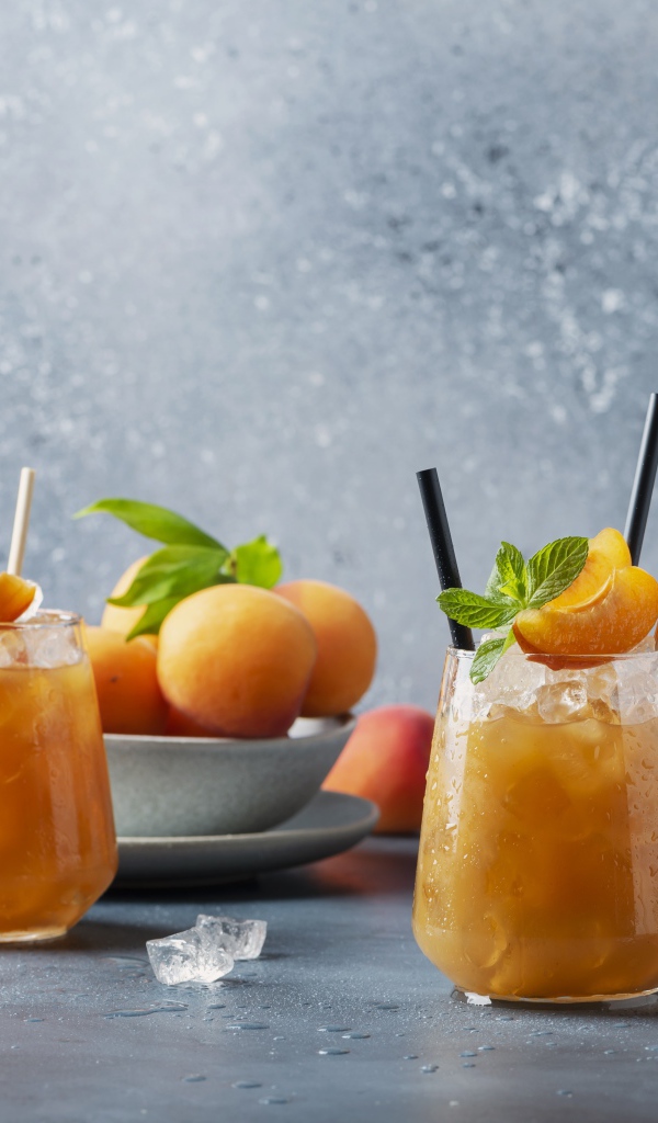 Холодный абрикосовый напиток со льдом в стаканах на столе со свежими абрикосами