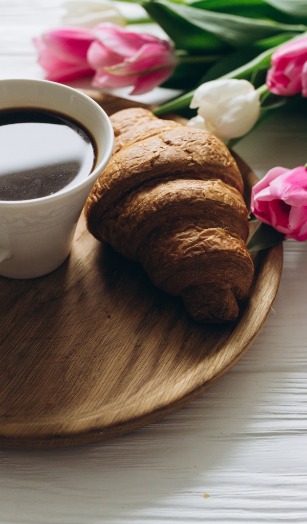 Чашка кофе и круассан на столе с букетом тюльпанов