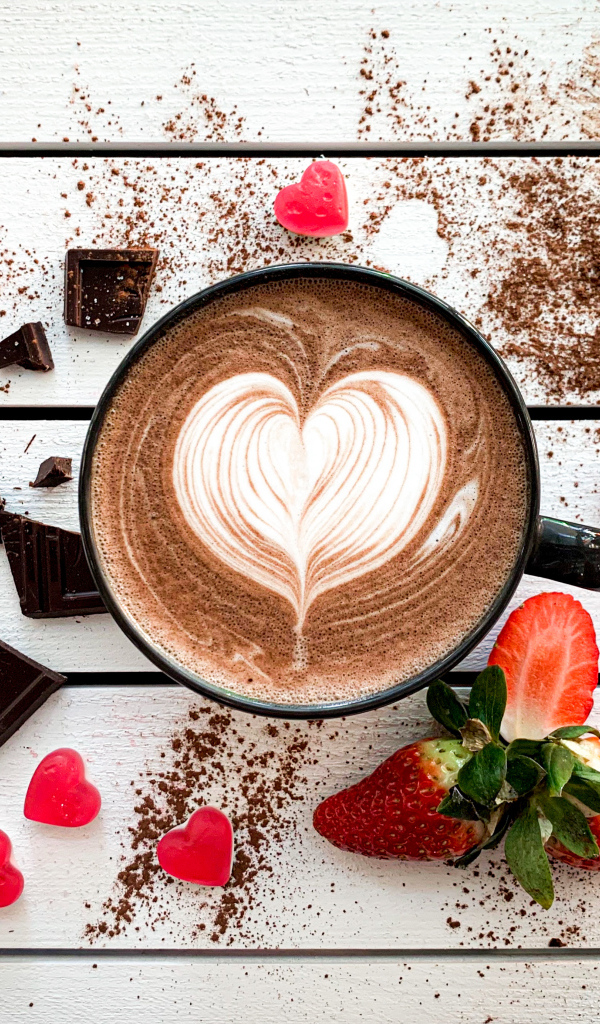 Чашка кофе с рисунком на пене на столе с шоколадом и клубникой 