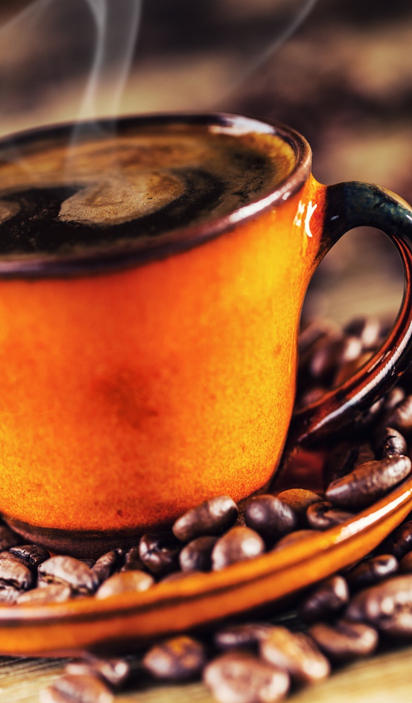 Оранжевая чашка горячего ароматного кофе на столе с зернами