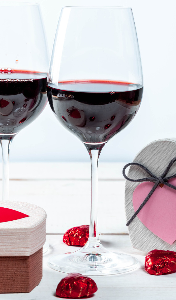 Две коробки с конфетами в форме сердца на столе с бокалами 