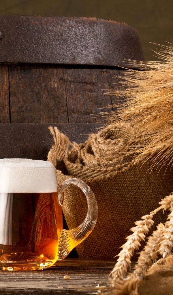 Два бокала пива на столе с колосьями пшеницы  и бочкой