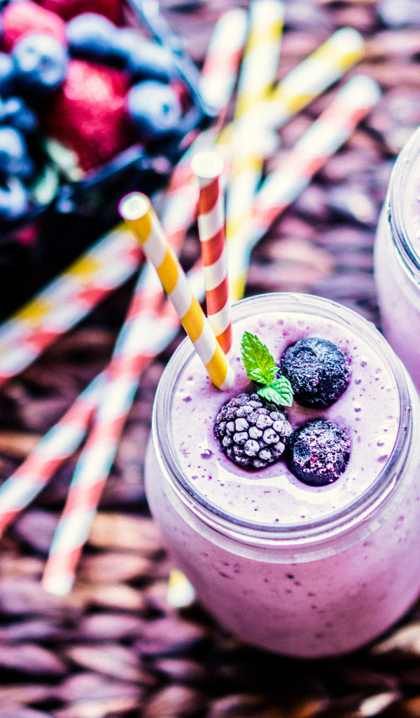 Две банки смузи с трубочками на столе с ягодами