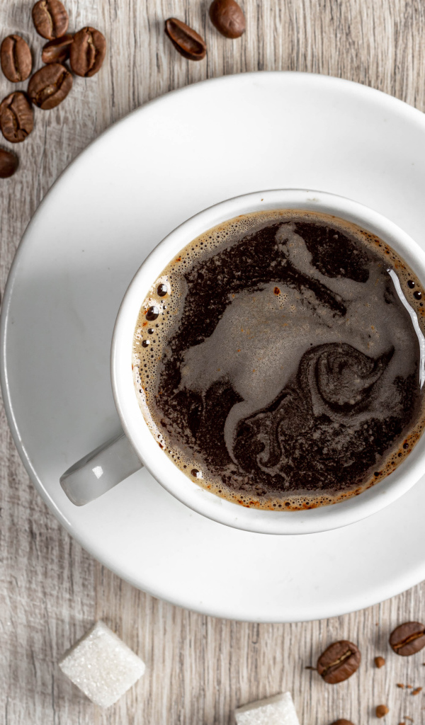 Белая чашка кофе на столе с зернами и сахаром